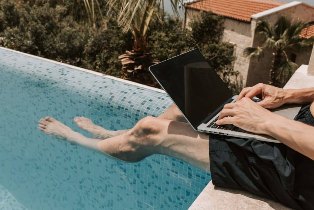 photo of man on laptop in pool as part of employee cost calculator blog post about gross capacity planning